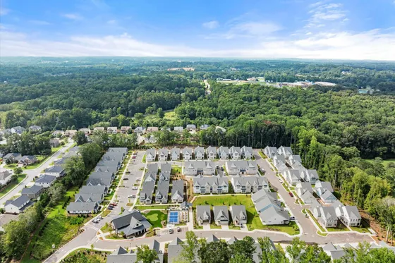 Scenic aerial view of a pristine residential area nestled amidst lush greenery, showcasing an inviting community with modern homes and well-maintained roads.