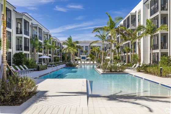 Luxurious apartment complex showcasing elegant architecture and a pristine swimming pool surrounded by lush palm trees and cozy lounge chairs.
