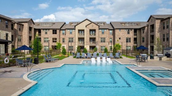 Luxurious apartment complex featuring a sparkling pool and elegant brick architecture, offering a resort-style living experience.