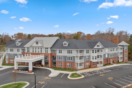 Elegant multi-story apartment building with classic architecture and modern design, featuring well-maintained landscaping and ample parking space, set against a tranquil, tree-lined backdrop.