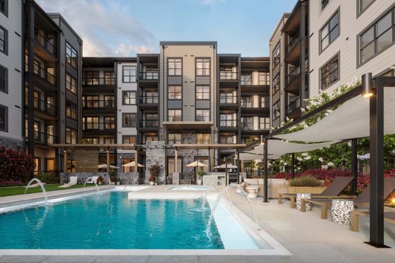 Modern apartment complex with elegant design featuring a sparkling outdoor pool, sun loungers, and lush landscaping for a luxurious lifestyle.