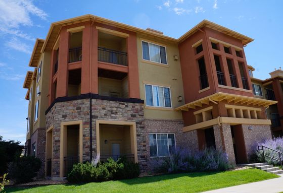 Charming multi-story apartment building with stylish stone and stucco facade, lush landscaping, and inviting balconies.