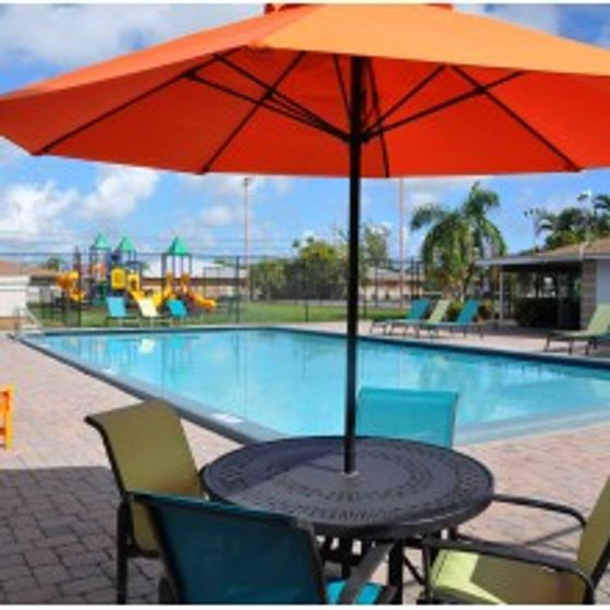 Pompano Palms Apartments, exterior, sparkling blue pool, picnic table with umbrella