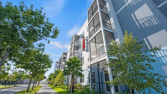 Modern apartment building exterior with spacious balconies, surrounded by lush greenery and a clear blue sky.