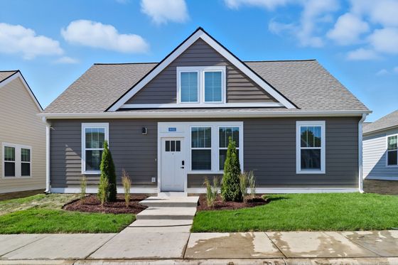 Charming single-story home with a grey facade, pristine lawn, and inviting front entrance under a clear blue sky.