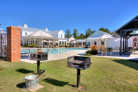 Inviting apartment complex showcasing a pristine swimming pool, cozy lounge chairs, and charming outdoor seating with umbrellas, perfect for relaxation and social gatherings.
