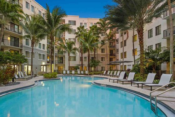 Luxurious apartment complex with a sparkling pool, lush palm trees, and elegant lounge chairs, offering a tropical oasis for relaxation.