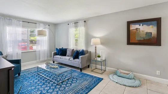 Inviting living room with modern decor featuring a cozy gray sofa, vibrant blue accents, and natural light streaming through sheer curtains.