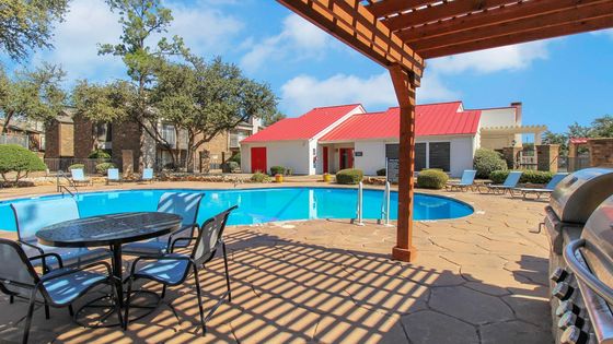 Charming outdoor area showcasing a sparkling blue pool surrounded by lounge chairs and vibrant greenery, complete with a nearby grill and shaded seating area, perfect for relaxation and entertaining.