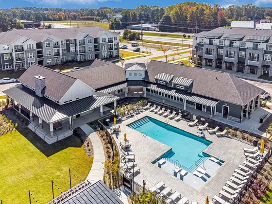 Stunning aerial view of modern apartment complex with elegant clubhouse, pristine swimming pool, and lush green surroundings.
