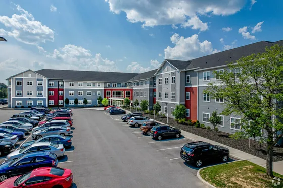 Modern apartment complex with stylish facade, ample parking, and vibrant surroundings under a bright blue sky.