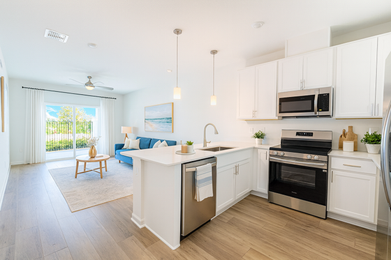 Bright and modern open-concept kitchen and living room with sleek appliances, stylish wooden flooring, and abundant natural light through patio doors.