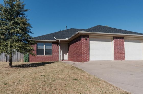 Inviting brick home with a two-car garage, surrounded by a well-maintained lawn and a single tree.