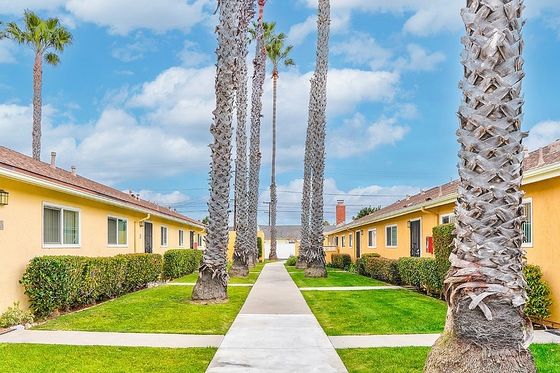 Charming apartment complex featuring vibrant yellow buildings with lush green lawns and towering palm trees, under a bright blue sky.