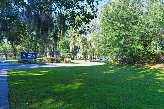 Inviting entrance of Ora Apartment Homes surrounded by lush greenery and trees.