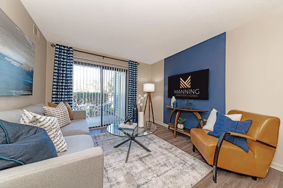 Cozy living room with modern decor, featuring a plush beige sofa, elegant blue accents, and large window doors leading to a patio.