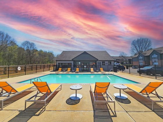 Luxurious apartment swimming pool with orange loungers set against a stunning sunset sky.
