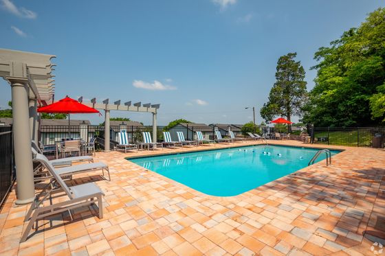 Charming outdoor pool area with sun loungers, red umbrellas, and lush greenery.
