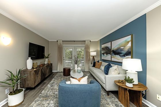 Chic living room with modern decor, featuring a cozy gray sofa, vibrant blue armchair, stylish artwork, and natural light through large windows.