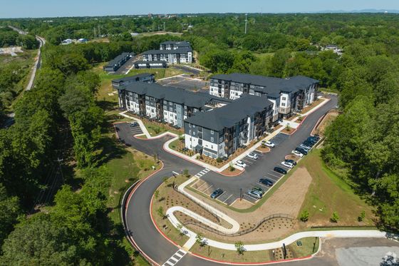 Aerial view of a modern apartment complex surrounded by lush greenery, showcasing stylish architecture and ample parking space.