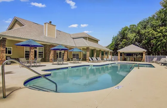 Inviting outdoor pool area with lounge chairs and umbrella-shaded seating, surrounded by lush greenery and a charming clubhouse.