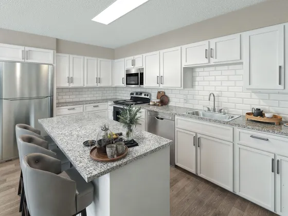 Modern kitchen featuring sleek white cabinetry, elegant granite countertops, stainless steel appliances, and cozy bar seating, perfect for culinary creations and gatherings.