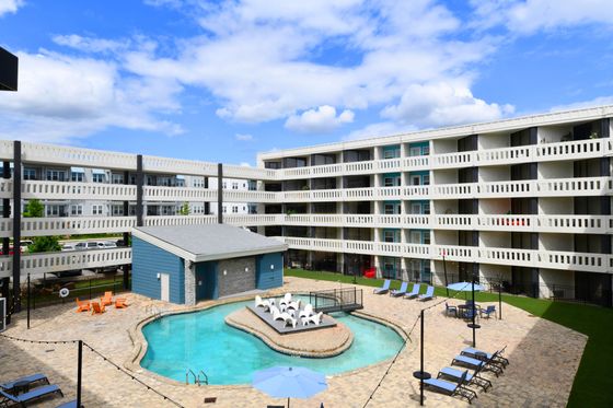 Vibrant apartment complex featuring a resort-style pool surrounded by modern lounge chairs and a stylish outdoor seating area.