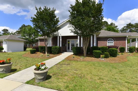 Charming brick exterior of a picturesque apartment building, surrounded by lush greenery and bright flowers, under a clear blue sky.