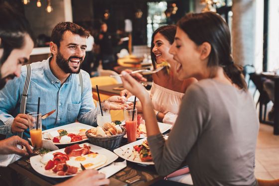 Joyful friends enjoying a delicious brunch with fresh juices, eggs, and salads in a cozy restaurant setting.