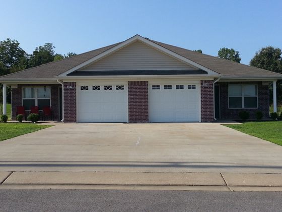 Charming brick home with dual garage doors, inviting porch, and lush green lawn.