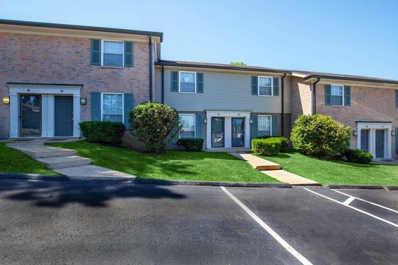 Charming townhouse with brick facade and lush green lawn, featuring front door entry and spacious windows.