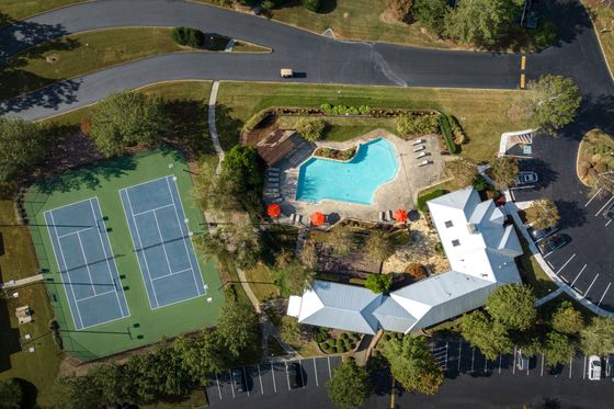 Aerial view of a luxurious apartment complex showcasing a pristine swimming pool, vibrant tennis courts, and lush landscaping.