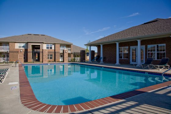 Inviting swimming pool area surrounded by elegant brick buildings and sun loungers under a clear blue sky.