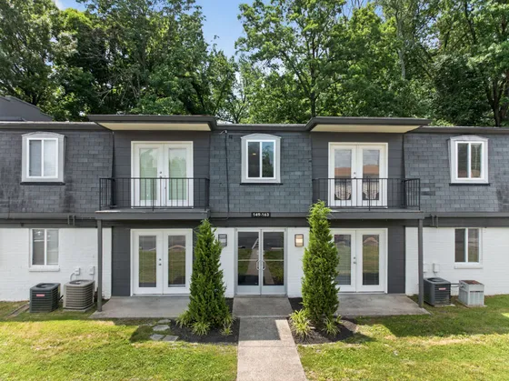 Charming two-story apartment building with a modern exterior, stylish balconies, and lush greenery in a serene wooded setting.