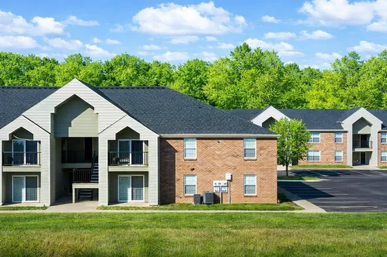 Charming brick apartment complex surrounded by lush greenery with ample parking and inviting balconies.