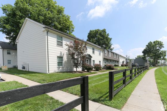 Charming suburban apartment complex with lush green lawns, a scenic walkway, and stylish white siding buildings under a bright blue sky.