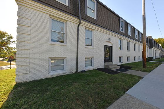 Charming apartment building with classic white brick exterior, nestled in a serene neighborhood with lush green surroundings.