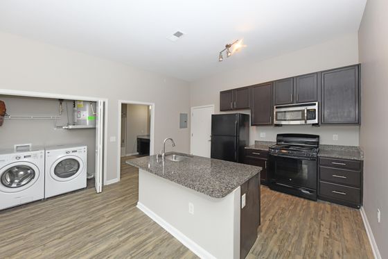 Modern kitchen with sleek granite countertops, dark cabinetry, and built-in laundry appliances accentuating stylish living space.