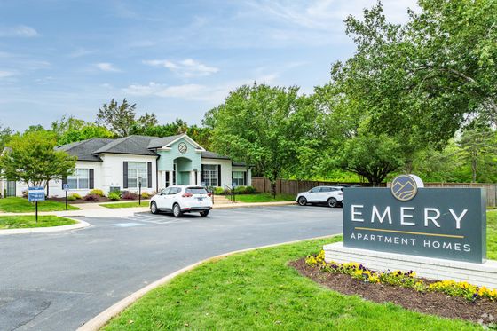 Inviting exterior of Emery Apartment Homes with lush greenery, accessible parking, and modern signage.