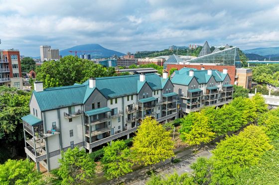 Charming townhouses with vibrant teal roofs, nestled in lush greenery, offering urban views and modern balconies.