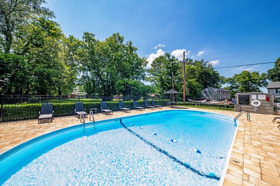 Inviting outdoor swimming pool surrounded by lush greenery and comfortable lounge chairs under a clear blue sky.