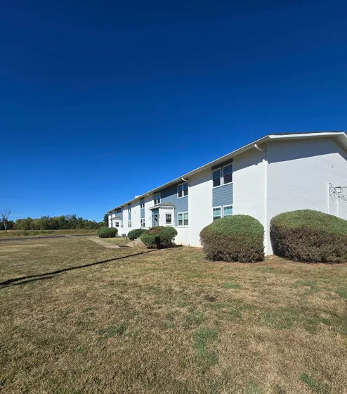 Charming brick apartment building with neatly trimmed lawns and spacious surroundings under a clear blue sky.