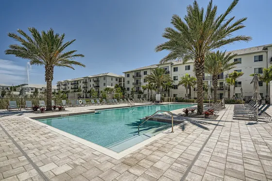 Elegant apartment complex with a luxurious outdoor pool surrounded by palm trees and lounge chairs, perfect for a relaxing retreat.