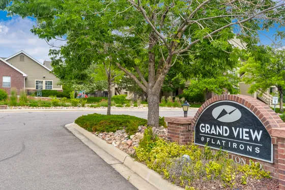 Charming entrance of Grand View at Flatirons, surrounded by lush greenery and well-maintained landscapes on a sunny day.