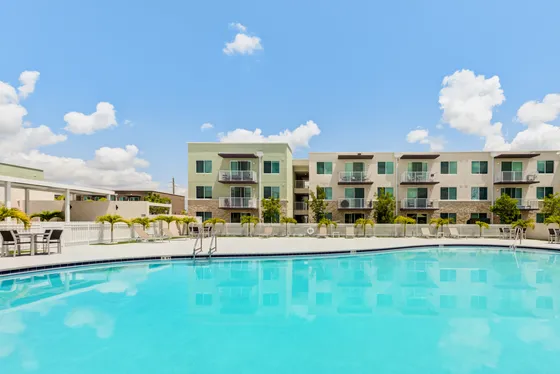 Modern apartment complex with elegant balconies overlooking a pristine, inviting swimming pool under a clear blue sky.