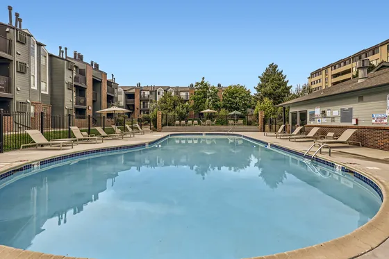 Inviting apartment complex with a refreshing swimming pool, surrounded by modern lounge chairs and lush greenery, perfect for relaxation and leisure.