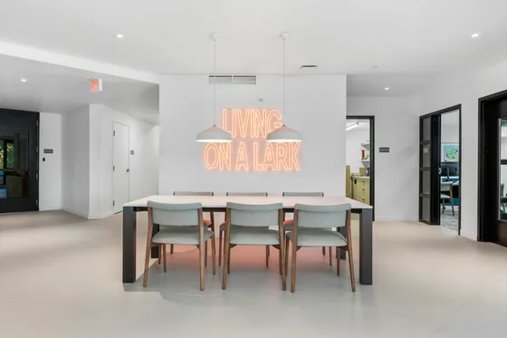 Modern dining area with sleek design, featuring a stylish table and chairs beneath contemporary pendant lighting, highlighted by a vibrant neon sign reading 'Living On A Lark'.