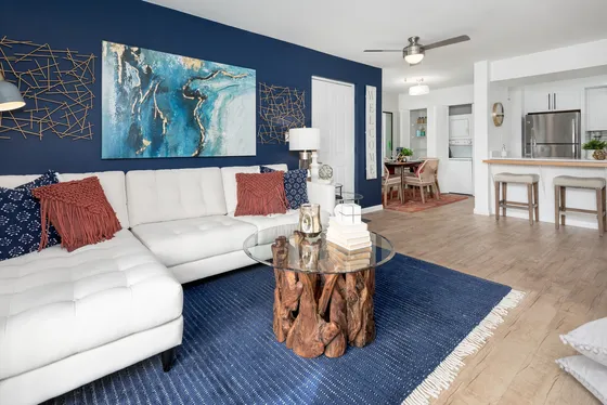 Chic living room featuring a modern white sectional, abstract artwork on a navy accent wall, and a unique wood coffee table with glass top.