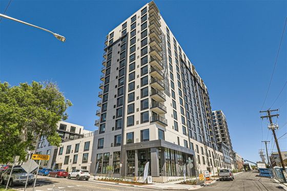 Modern high-rise apartment building set against a clear blue sky, featuring sleek design and private balconies.