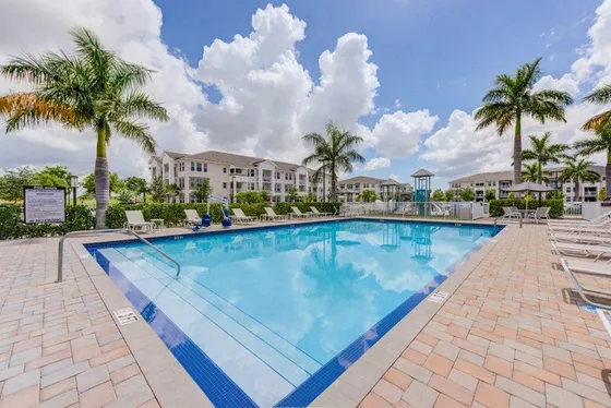 Luxurious apartment complex featuring a crystal-clear pool surrounded by elegant palm trees under a bright blue sky.